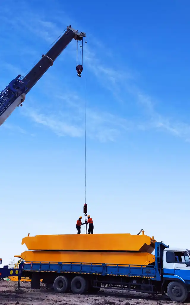 A mobile crane lifting a yellow steel load from a flatbed truck