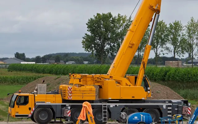 A yellow all-terrain crane with outriggers set on a construction site