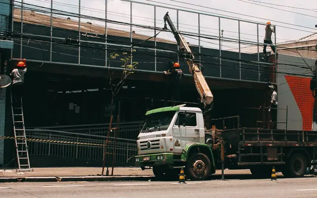 A boom truck with its crane lifting materials up to workers at a building on a city street