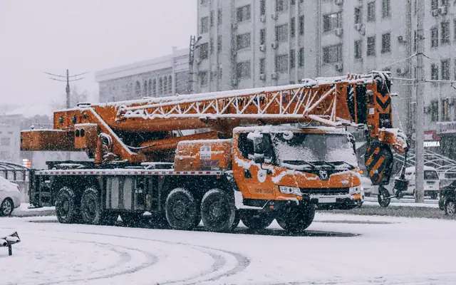 An orange hydraulic truck crane parked on a snowy city street