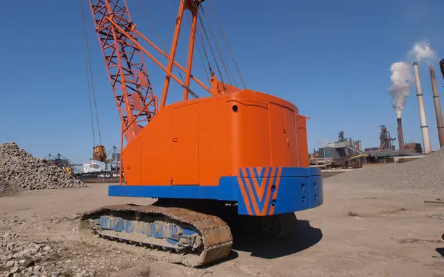 An orange lattice-boom crawler crane on tracks in an industrial yard