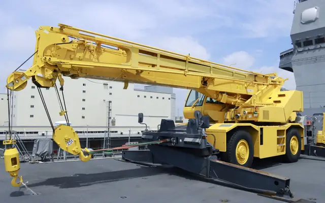 A yellow rough-terrain crane with large tires, a single cab and its outriggers extended